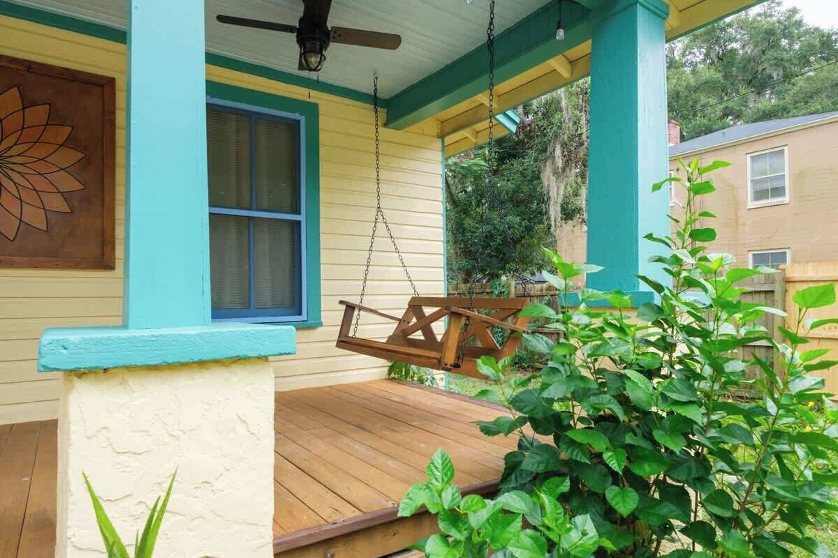 A porch with a swing, a ceiling fan, and a window with blue trim.