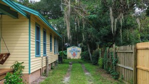 A yellow house with a porch and a swing, surrounded by a wooden fence and dense greenery. - Gville and Chill House (Gainesville)