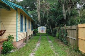 A yellow house with a porch and a swing, surrounded by a wooden fence and dense greenery. - Gville and Chill House (Gainesville)