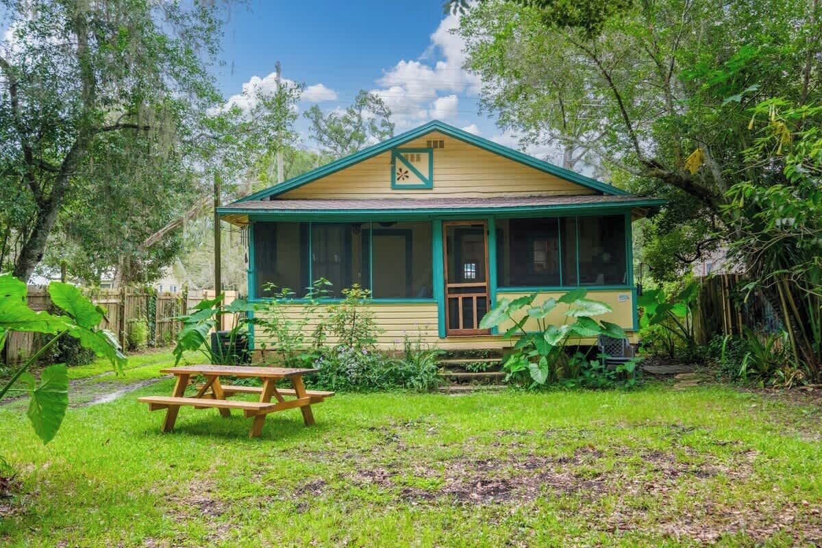 A single-story house with a porch, surrounded by lush greenery.