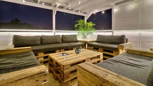A cozy seating area with a sofa and chairs, wooden pallets as tables, and a large window with a night view.