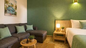 Una habitación con un sofá, una mesita redonda con una planta, una lámpara y una cama con cabecera de madera.