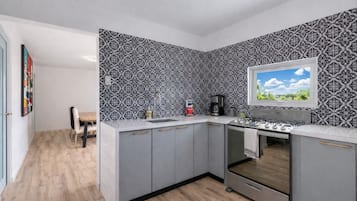 Una cocina moderna con armarios grises, estufa empotrada y ventana con vista al cielo.