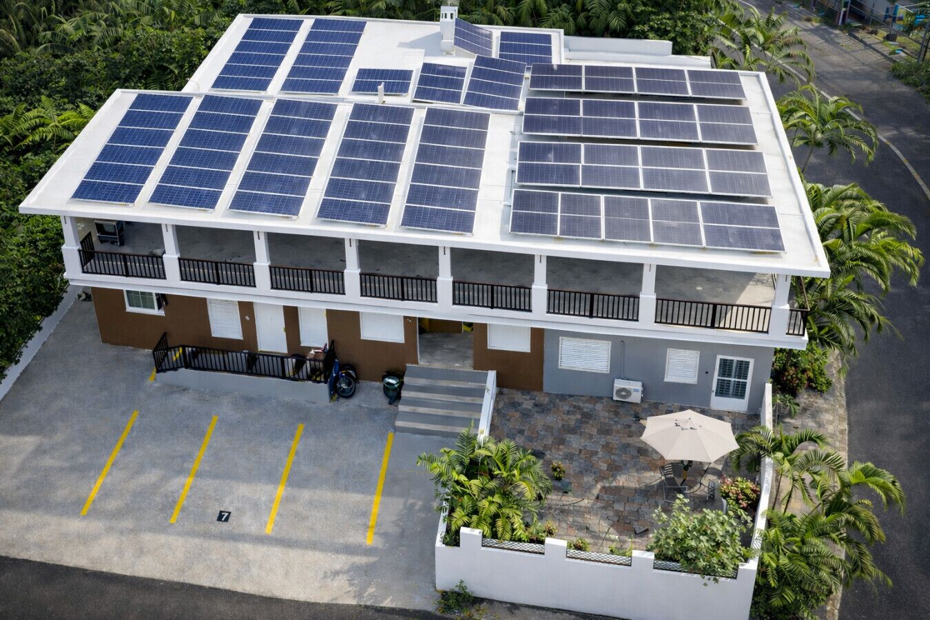 A multi-story building with solar panels on the roof, a parking area, and a small garden with plants.