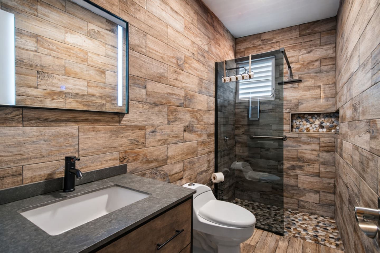 A bathroom with a wooden wall design, a sink, a toilet, and a shower area.