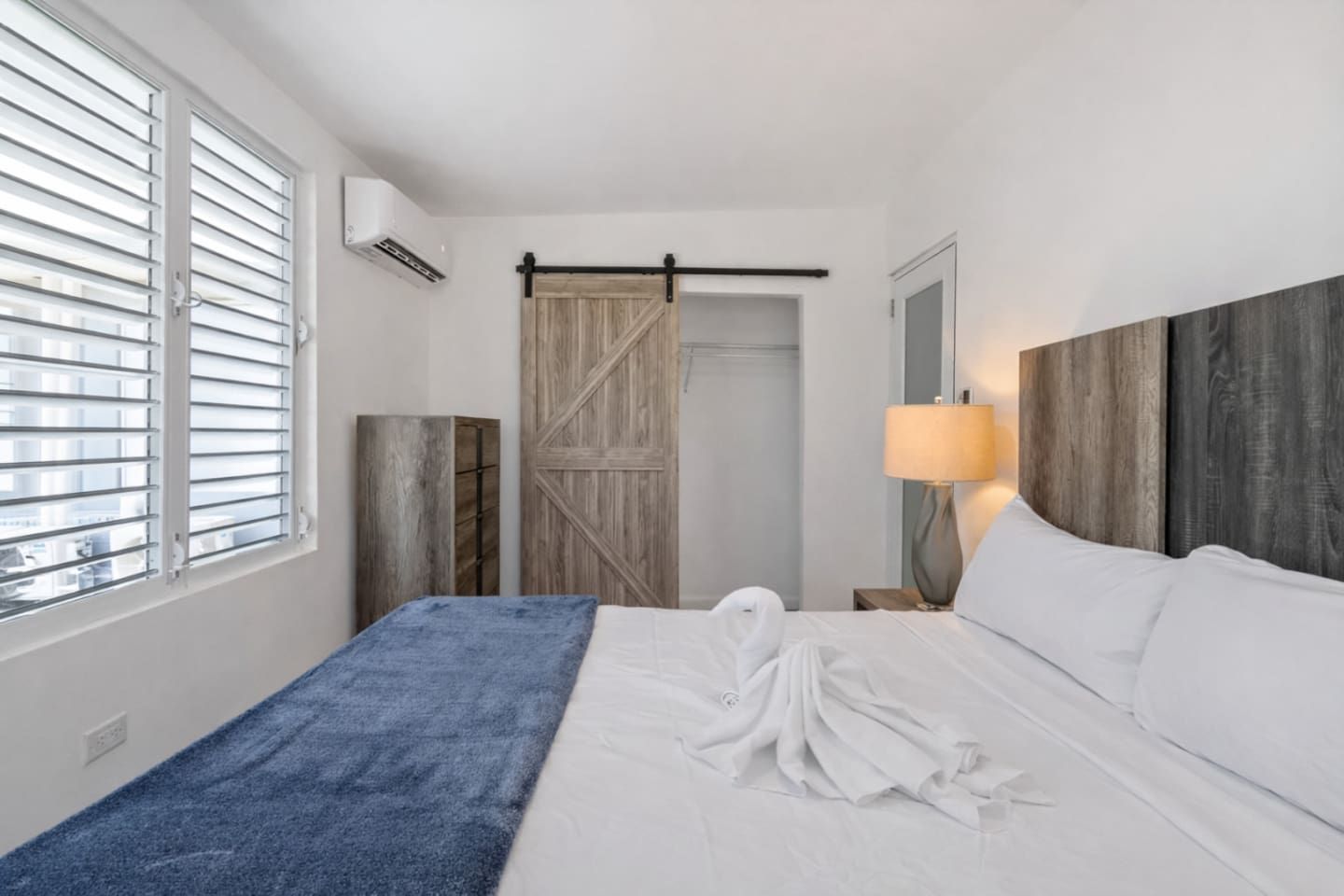 Una habitación de hotel con una cama, una toalla azul, un armario de madera, una puerta corredera estilo granero y una lámpara de noche.