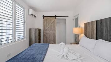 Una habitación de hotel con una cama, una toalla azul, un armario de madera, una puerta corredera estilo granero y una lámpara de noche.