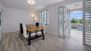 A dining area with a wooden table and chairs, a ceiling light, and a view through a door to an outdoor balcony. - Top Floor Gem | Huge Balcony + Parking + Nature (Ceiba)
