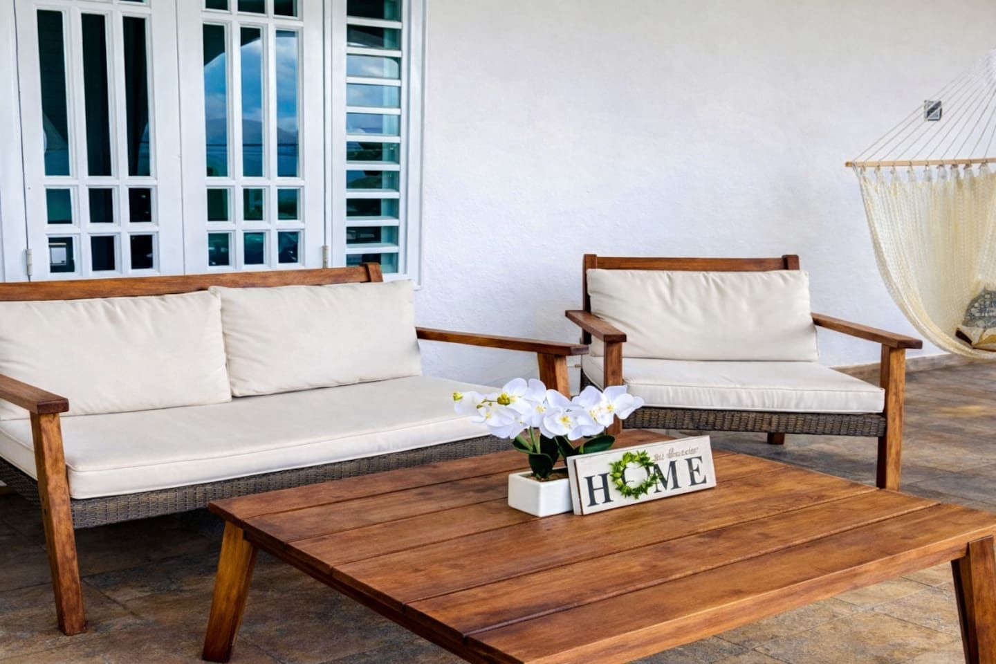 A wooden coffee table with a 'HOME' sign, two wooden chairs with cushions, and a white sofa.