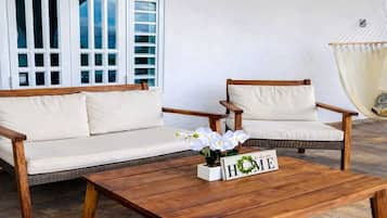 A wooden coffee table with a 'HOME' sign, two wooden chairs with cushions, and a white sofa.