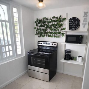 Una cocina con estufa negra, microondas, cafetera y una planta colgante en la pared.