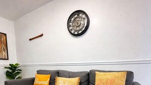 Un canapé gris avec trois coussins, une horloge murale et une plante.