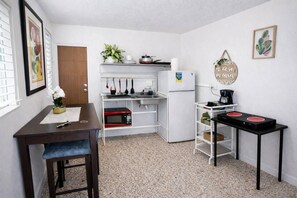 Una cocina compacta con refrigerador, microondas y una pequeña mesa de comedor con una silla.