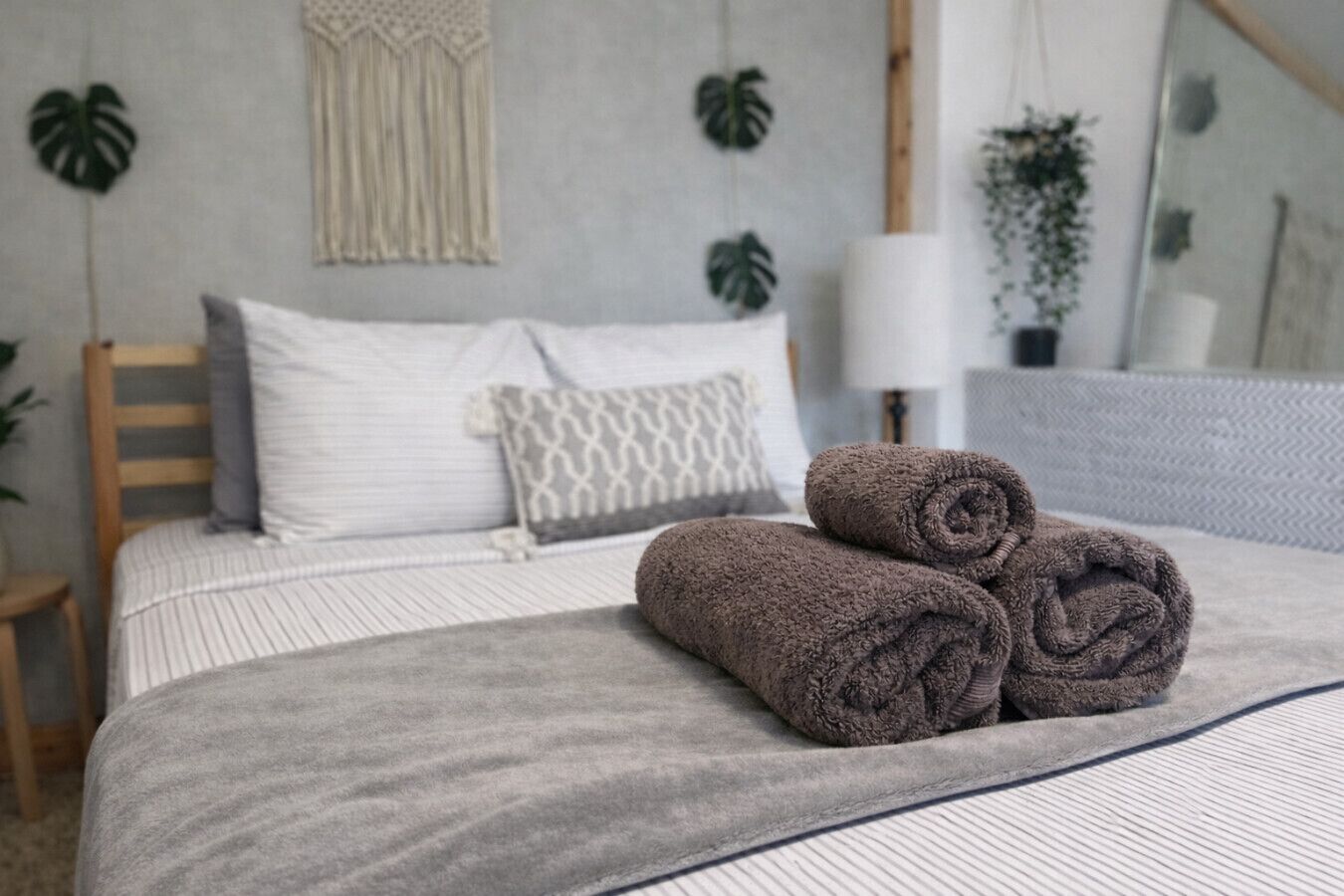 Een net opgemaakt bed met opgerolde handdoeken, een bedlampje en een spiegel aan de muur.