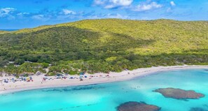 Una playa con aguas turquesas cristalinas, una orilla arenosa y una colina verde exuberante al fondo.