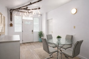 Ein modernes Interieur mit einem Glastisch, grauen Stühlen, einer Zimmerpflanze und einer weißen Tür mit Fenster.
