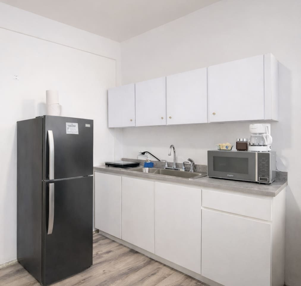 A compact kitchen with a refrigerator, microwave, sink, and cabinets.
