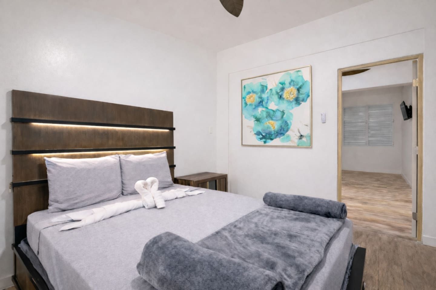 A modern bedroom with a bed, bedside tables, a painting, and a wooden floor.