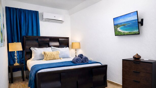 Een slaapkamer met een bed, nachtlampjes, een dressoir, een airconditioning en een aan de muur bevestigde televisie.