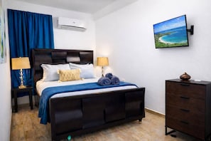 Ein Hotelzimmer mit einem Bett, Nachttischlampen, einem Schminktisch, einer Klimaanlage und einem an der Wand montierten Fernseher.