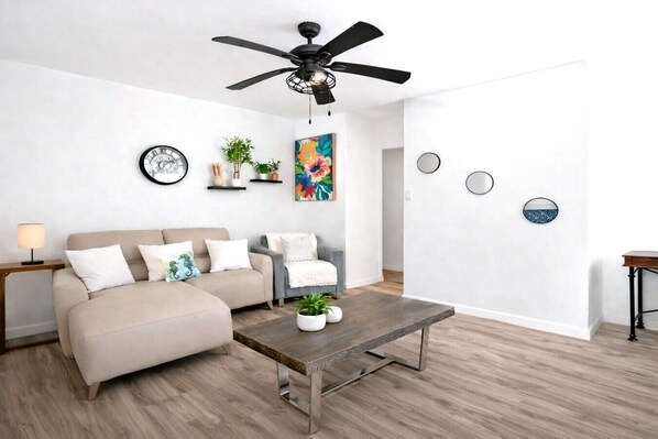 Een moderne woonkamer met een plafondventilator, een bank, een salontafel en decoratieve objecten aan de muren.