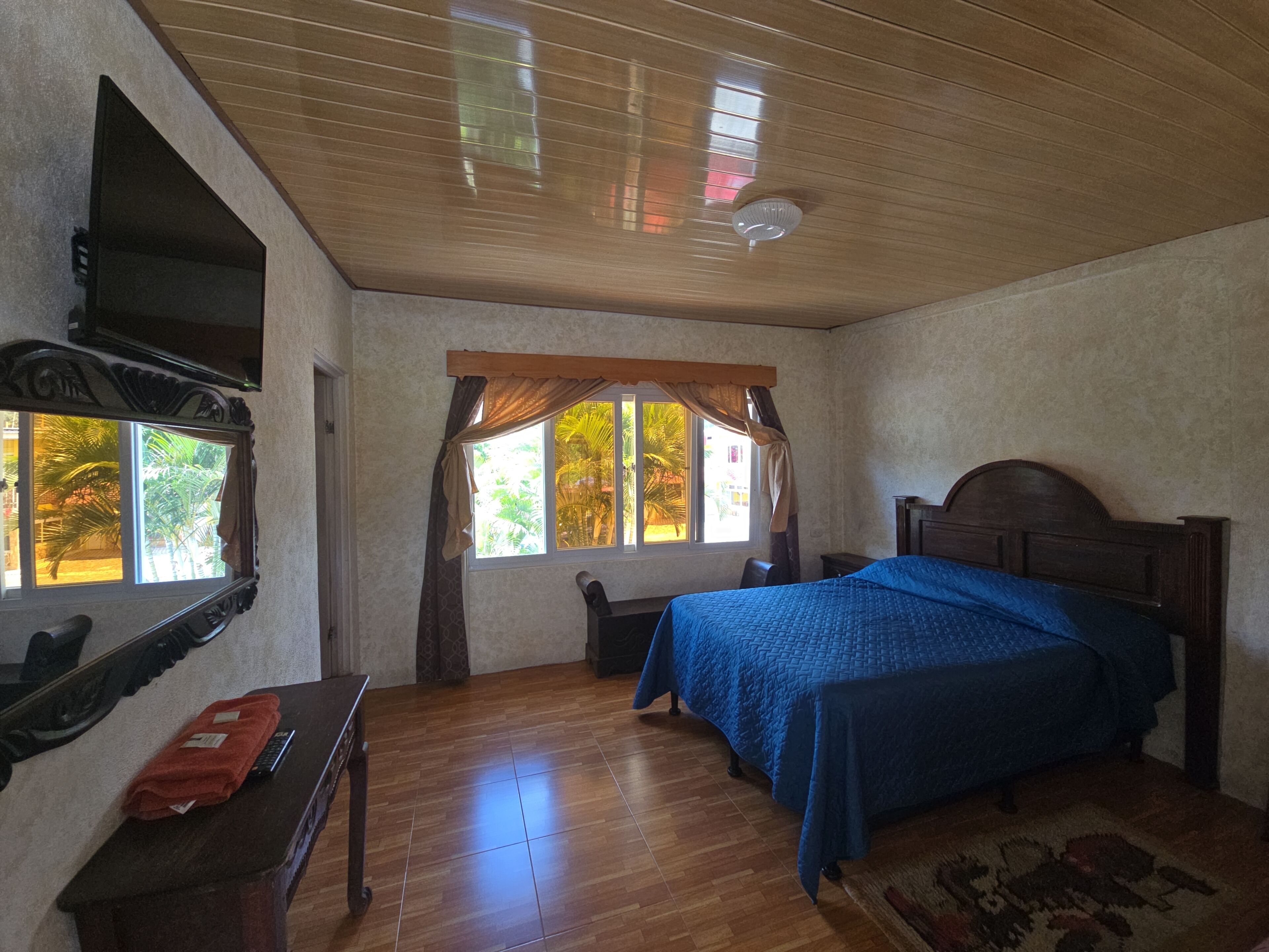 Ein Zimmer mit einem Bett, einem Schreibtisch, einem Stuhl, einem Vorhangfenster und einem Deckenventilator.