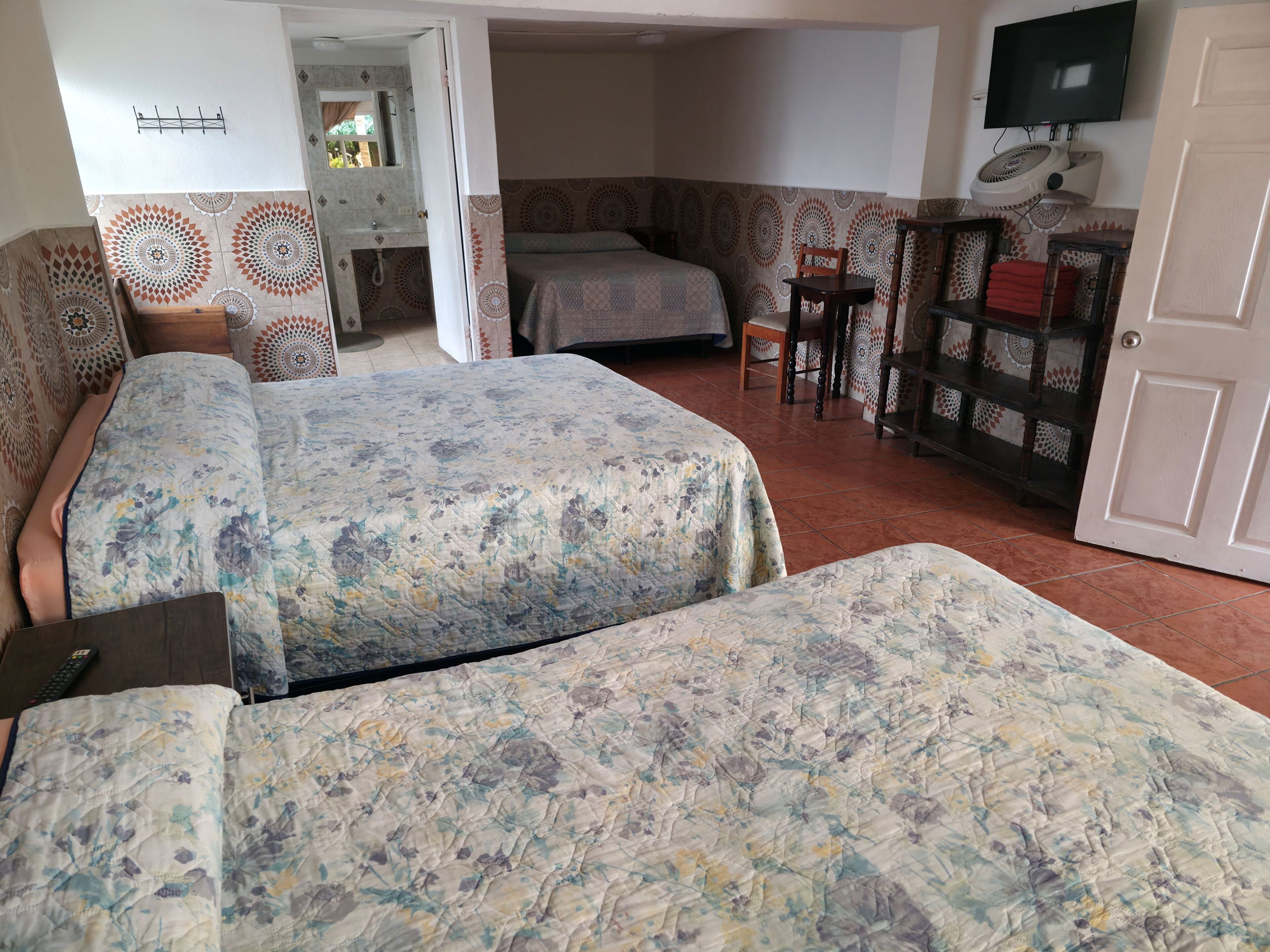 Una habitación con dos camas, televisión, ventilador y un armario de madera.