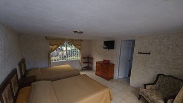 A room with two beds, a wooden dresser, a chair, a television, and a door.