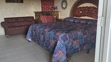 Une chambre à coucher avec un lit, une tête de lit en bois, une cheminée en briques rouges, un banc en bois et un miroir fixé au mur.