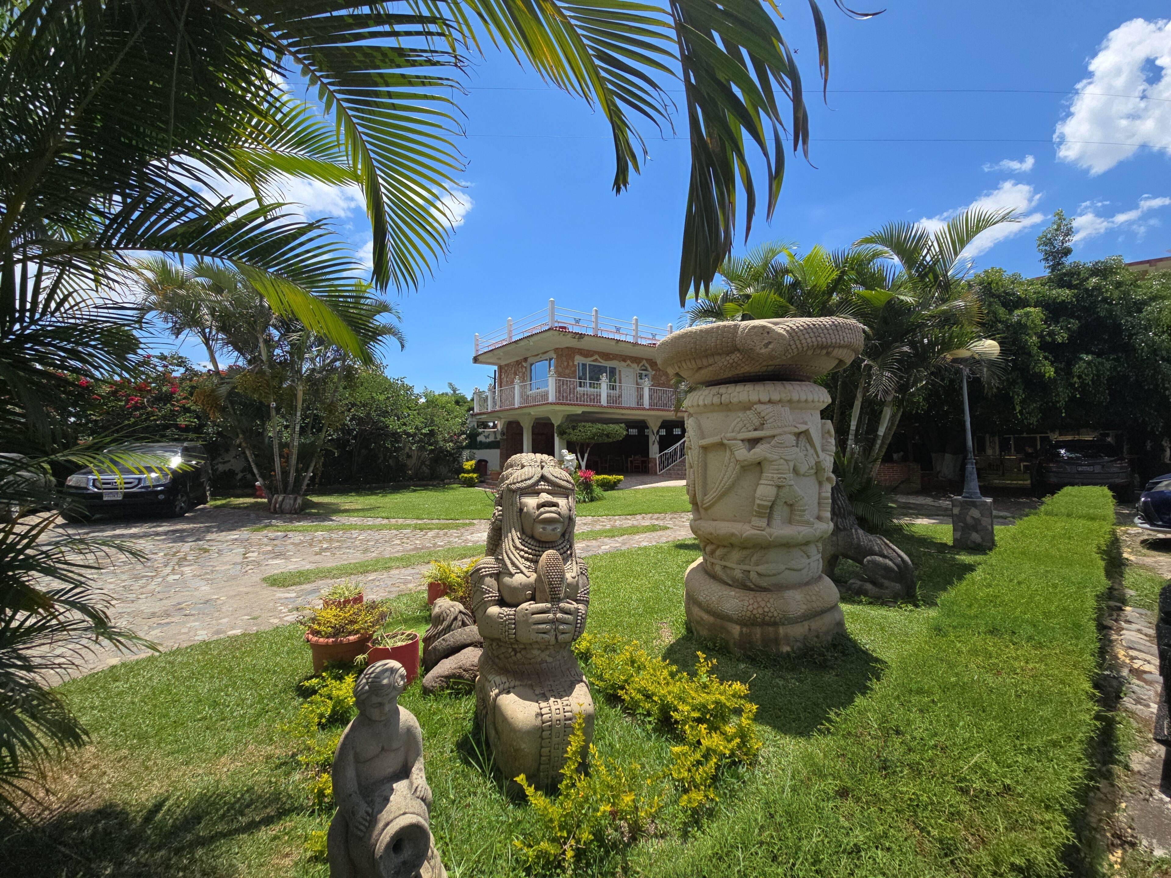 A garden with statues, a stone pillar, and a house with a balcony.