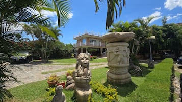 Un jardin agrémenté de statues, un pilier en pierre et une maison dotée d’un balcon.