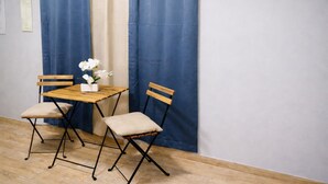 A room with a wooden table and two chairs, a vase with flowers, and blue curtains. - Solar Island Base | WiFi, Parking and Near Ferry (Ceiba)