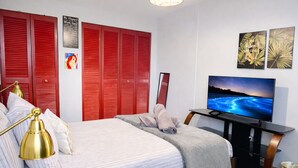 A bedroom with a bed, a TV, red shutters, and artwork on the wall. - Solar Island Base | WiFi, Parking and Near Ferry (Ceiba)