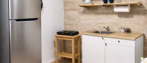 A kitchen with a stainless steel refrigerator, wooden countertop, and a small wooden stool.