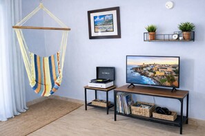 Ein Zimmer mit einer Hängematte, einem gerahmten Bild, einem Fernseher und Regalen mit Pflanzen und Büchern.