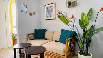 A cozy room with a sofa, two small tables, a large potted plant, and wall decorations including a framed picture and a framed certificate.