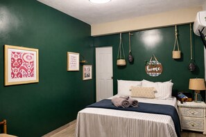 Camera da letto con un letto, un comodino, una lampada e decorazioni murali tra cui un cartello con la scritta 'home' e quadri incorniciati.