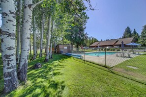 Ein umzäunter Hinterhof mit Swimmingpool, überdachter Terrasse und einem Gebäude mit braunem Dach.