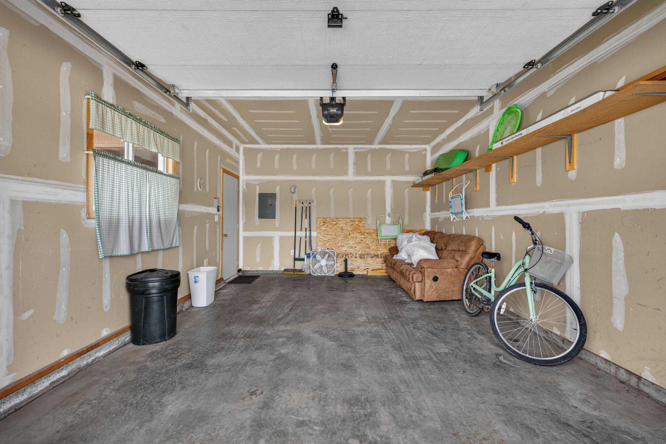 A garage with a concrete floor, a brown sofa, a bicycle, and a fan.