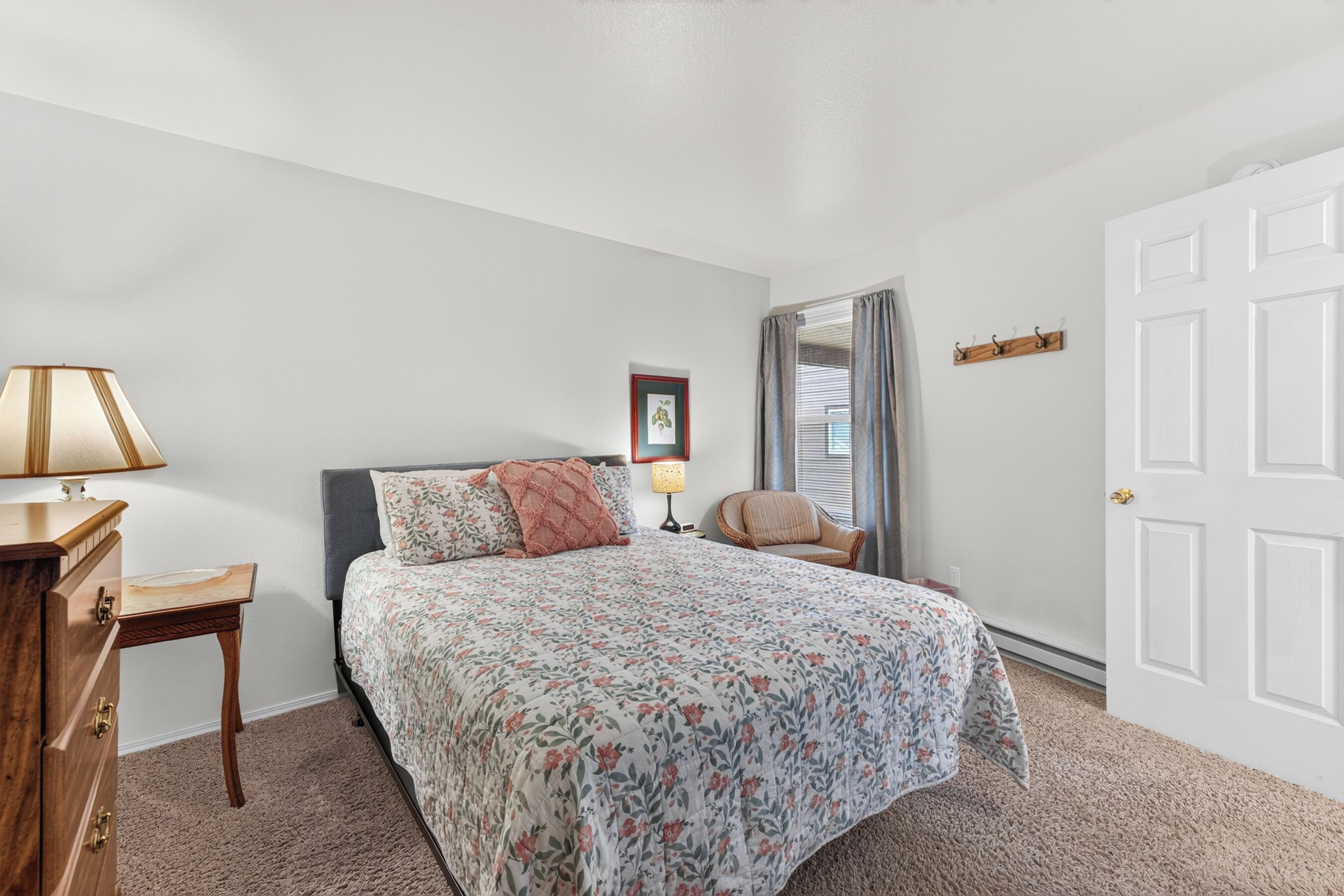 Une chambre à coucher avec un lit, une chaise, un bureau, une lampe, un porte-manteau et une porte.