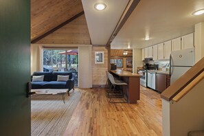 A modern kitchen with wooden cabinets, a refrigerator, and a dining area with a bar stool. - 16 Pole House - Hot Tub, SHARC Passes, Mountain Getaway (Bend)