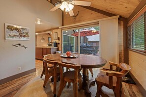 Ein Holztisch mit Stühlen, ein Deckenventilator und Blick ins Freie durch eine Glastür.