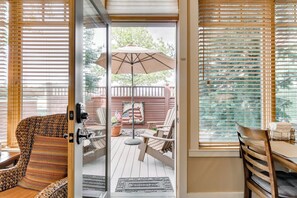 Eine Glastür führt zu einer Terrasse mit Holzdeck, Gartenmöbeln und einer Flagge.