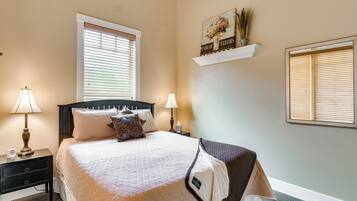 Une chambre à coucher bien rangée, avec un lit, deux tables de chevet dotées de lampes, une table de nuit, une fenêtre avec des stores et une étagère murale agrémentée d’objets décoratifs.