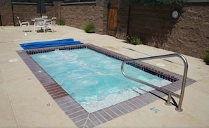 Ein rechteckiger Pool im Freien mit einer Metallleiter, umgeben von einer Ziegelumrandung und einer gefliesten Kante.