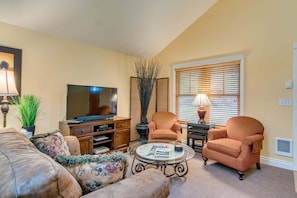 A living room with a television, two armchairs, a coffee table, and a window with blinds.