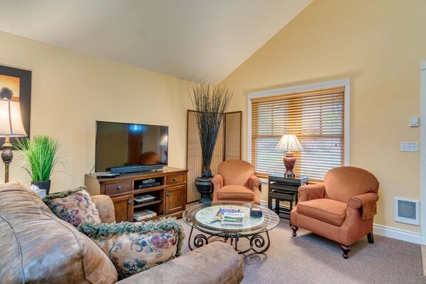 A living room with a television, two armchairs, a coffee table, and a window with blinds.