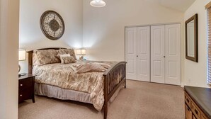 Ein Schlafzimmer mit einem Bett, Nachttischen, einem Kleiderschrank, einer Pendelleuchte und einer Wanddekoration.