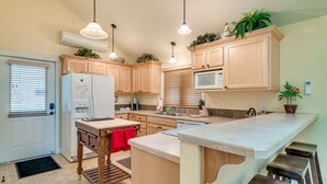 Eine Küche mit Holzausstattung, einem Kühlschrank, einer Mikrowelle und einem Spülbecken. An der Arbeitsplatte befinden sich Pendelleuchten und ein Blumentopf.