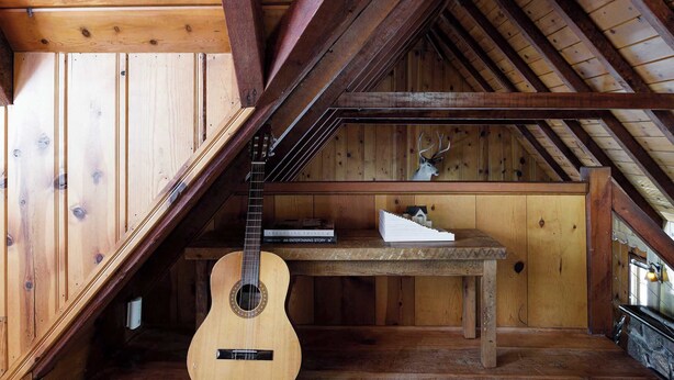 A wooden interior with a sloped ceiling, a guitar leaning against the wall, and a table with books and a model house. - The Writer's Cabin in Lake Arrowhead Woods (Lake Arrowhead)